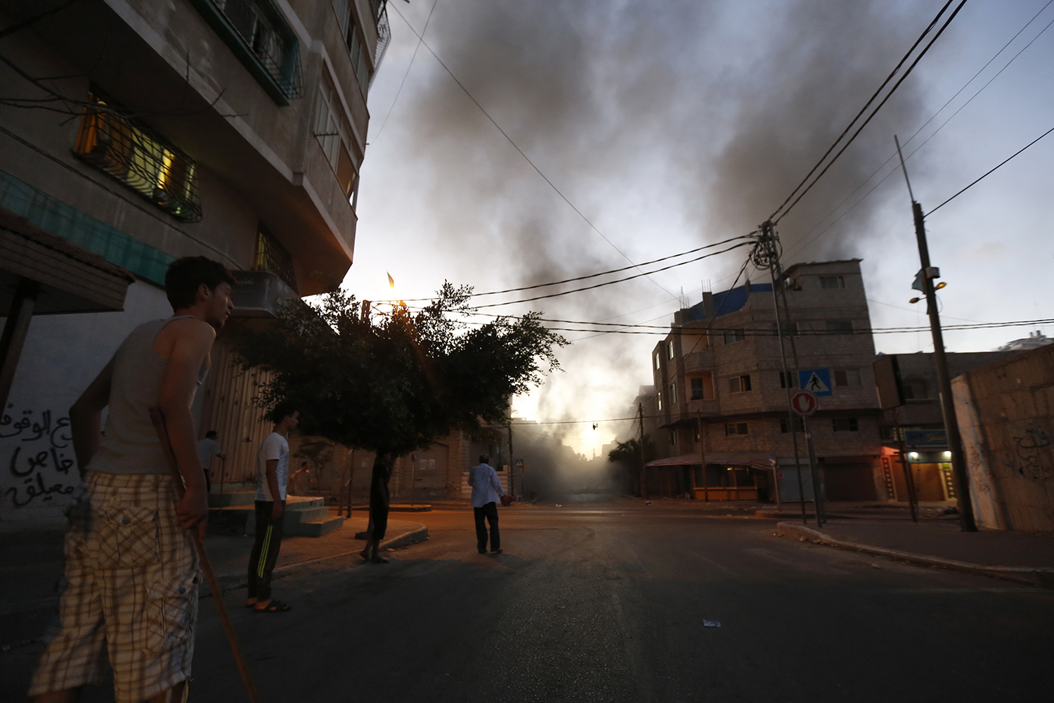 Palestinians stand looking at smoke billowing from a nearby building hit by an Israeli air strike in Gaza City on July 13, 2014. Photo: Getty Images